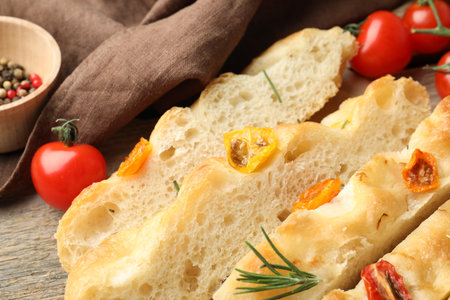 Cut delicious focaccia with tomatoes and rosemary on table, closeupの写真素材