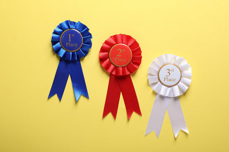 Different award ribbons on yellow background, flat lay