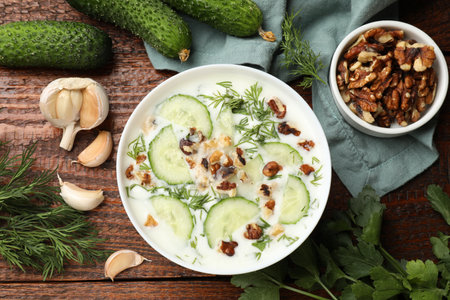 Tasty cucumber soup with dill, nuts and garlic on wooden table, flat layの写真素材