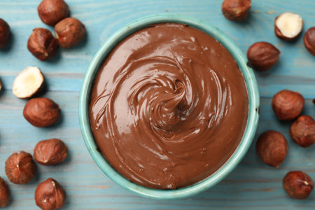 Tasty chocolate hazelnut spread and nuts on blue wooden table, flat layの写真素材