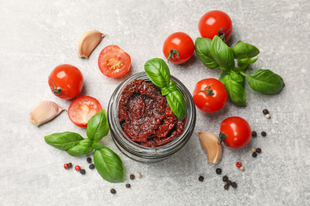Delicious sun dried tomatoes, fresh vegetables, basil and garlic on light grey table, flat lay