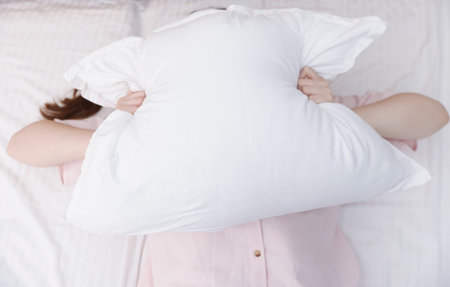 Woman covering herself with pillow on bed at home, above view. Insomnia problem