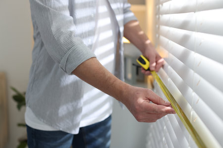 Man measuring white window blinds with tape indoors, closeupの写真素材