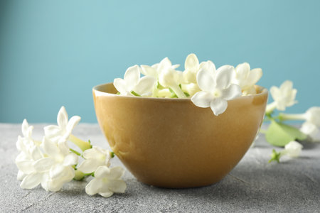 Beautiful flowers in bowl on grey table against light blue background, closeupの写真素材