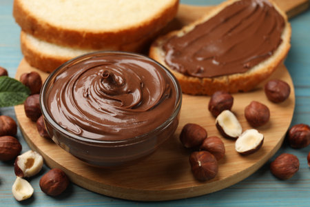 Chocolate hazelnut spread in bowl, nuts and toasts on light blue wooden table, closeupの写真素材