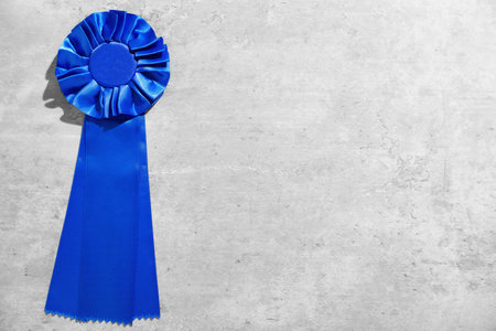 Blue award ribbon on light grey table, top view. Space for text