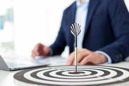 Man working on laptop at table, focus on dartboard with arrow indoorsの写真素材