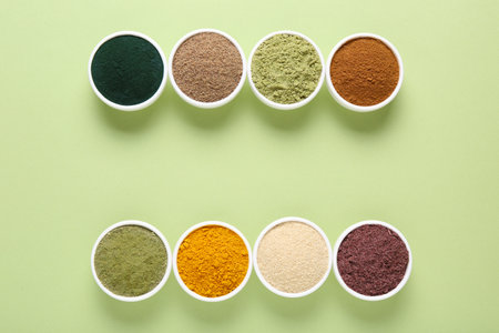 Different superfood powders in bowls on pale green background, flat lay. Space for textの写真素材