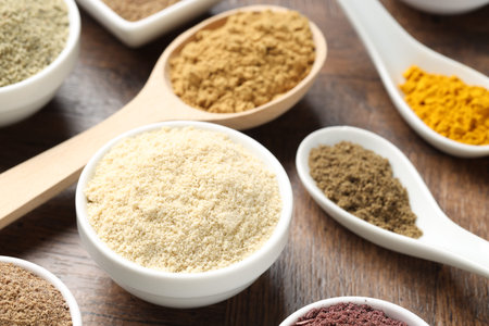 Different superfood powders in bowls and spoons on wooden table, closeup