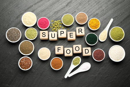 Different superfood powders and words made of cubes on black table, flat layの写真素材