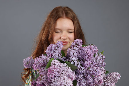 Beautiful teenage girl with bouquet of lilac flowers on grey backgroundの写真素材
