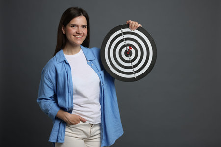 Targeting. Smiling woman with dart board on grey background