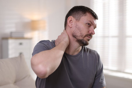 Man suffering from neck pain at homeの写真素材