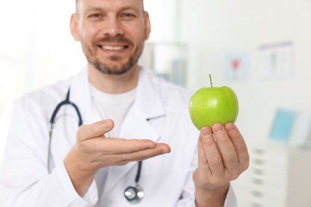 Nutritionist with green apple and stethoscope in clinic, selective focusの写真素材