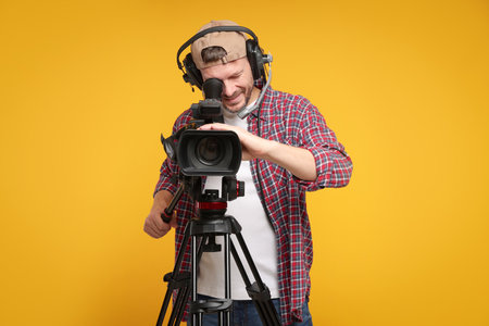 Man with professional video camera and headset on orange backgroundの写真素材