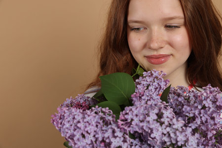 Beautiful teenage girl with bouquet of lilac flowers on beige background, closeup. Space for textの写真素材
