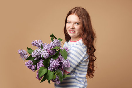 Smiling teenage girl with bouquet of lilac flowers on beige backgroundの写真素材