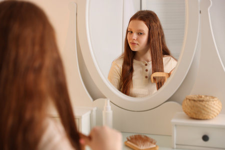 Beautiful teenage girl brushing her hair with comb near mirror at home, selective focusの写真素材