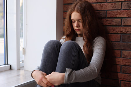 Sad teenage girl near window at homeの写真素材