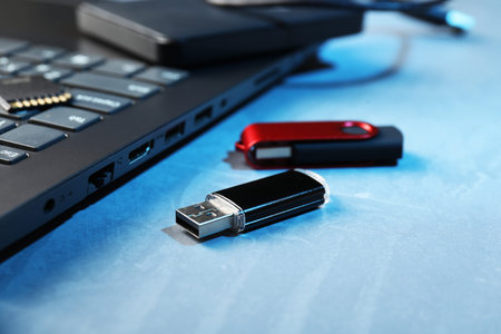 Usb flash drives and laptop on blue textured table, closeup