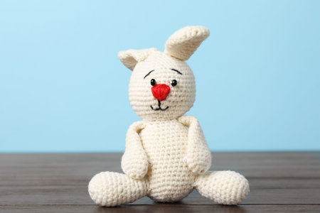 Cute knitted toy bunny on wooden table against light blue backgroundの写真素材