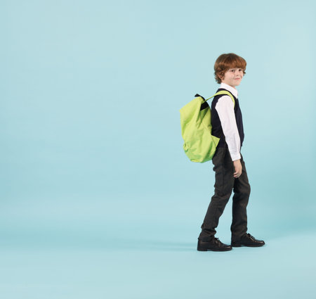 Cute schoolboy with backpack on light blue background, space for text
