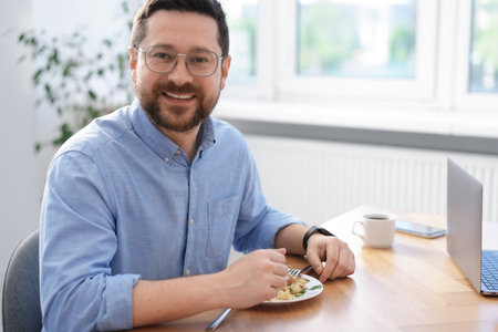 Man with meal at table during lunch break in office. Space for textの写真素材