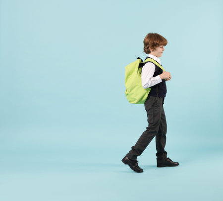 Cute schoolboy with backpack on light blue background, space for textの写真素材