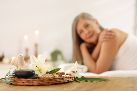 Senior woman relaxing on massage couch indoors, focus on different spa products and lily flowersの写真素材