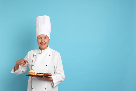 Professional pastry chef pointing at desserts on light blue background. Space for textの写真素材