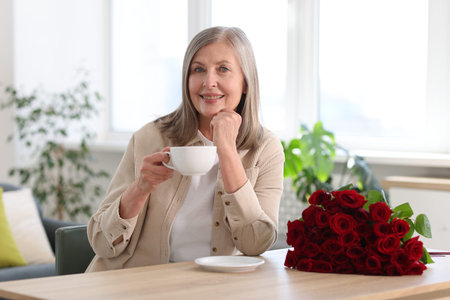 Smiling woman with bouquet of roses drinking at table indoorsの写真素材