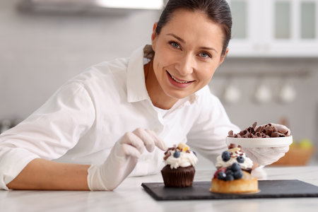 Confectioner decorating cupcake with piece of chocolate at tableの写真素材