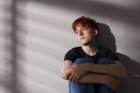 Teen problems. Depressed teenage boy near gray wall, space for text