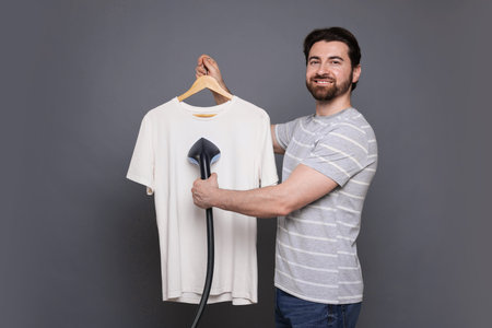 Man steaming t-shirt with stand steamer on grey backgroundの写真素材