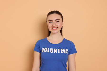 Portrait of smiling woman in t-shirt with word Volunteer on beige backgroundの写真素材