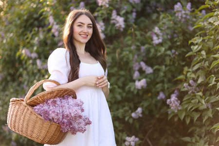 Smiling woman with basket of lilac flowers near bush outdoorsの写真素材