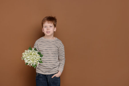 Boy with bouquet of beautiful lily-of-the-valley flowers on brown background. Space for text