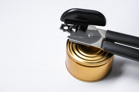 Can opener and tin on white wooden table, closeup. Space for textの写真素材