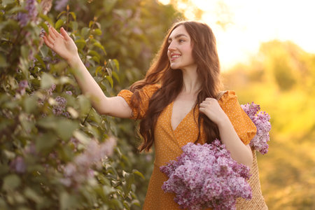 Smiling woman with bag of lilac flowers near bush outdoors in morningの写真素材