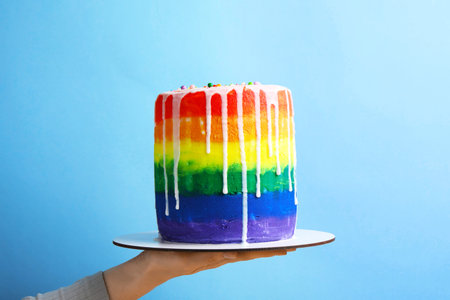 Woman with delicious rainbow cake on light blue background, closeup