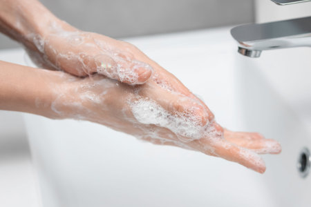Woman washing hands at sink in bathroom, closeup