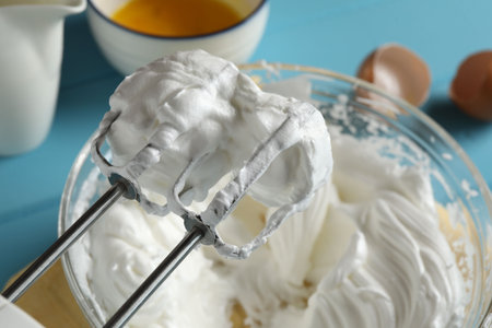 Hand mixer with whisks and whipped cream on light blue table, closeupの写真素材