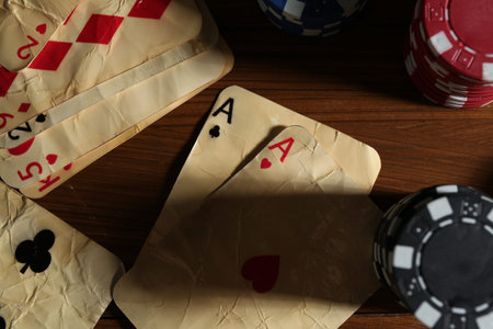 Old vintage playing cards and poker chips on wooden table, flat lay