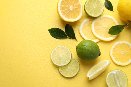 Fresh lemons, limes and green leaves on yellow background, flat lay. Space for textの写真素材