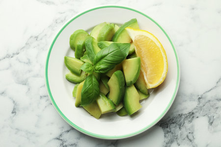 Tasty ripe green avocado, basil and lemon on white marble table, top viewの写真素材