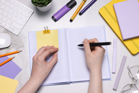 Woman with planner and stationery at light marble table, top view