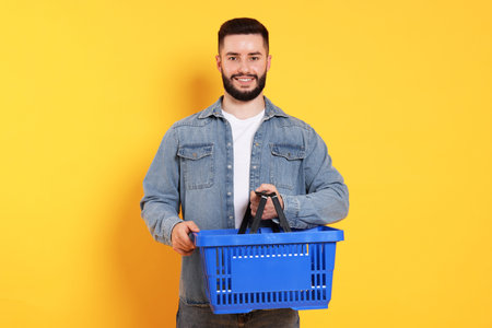 Man with empty shopping basket on orange background