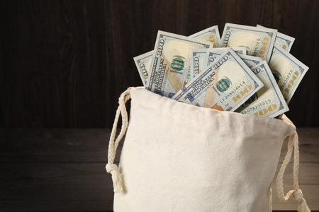 Money bag with dollar banknotes on wooden table, closeup. Space for textの写真素材