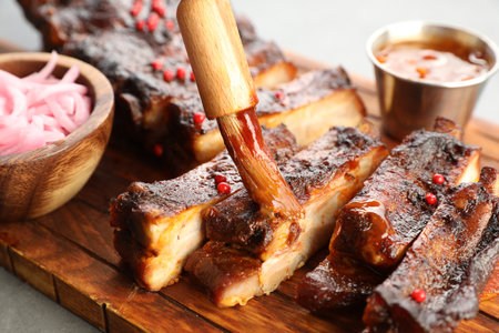 Spreading sauce with brush onto delicious spare ribs at grey table, closeupの写真素材