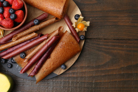 Delicious fruit leather rolls and berries on wooden table, flat lay. Space for textの写真素材